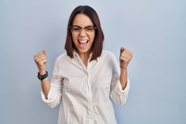 Young hispanic woman standing over white background celebrating surprised and amazed for success with arms raised and eyes closed. winner concept. 