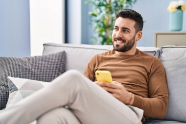 Evdeki kanepede oturan, akıllı telefon kullanan genç bir İspanyol.