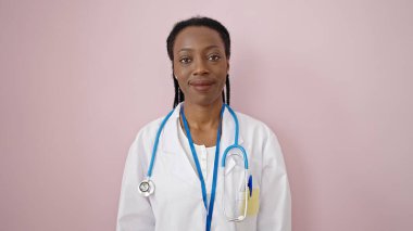 Afro-Amerikalı kadın doktor, pembe arka planda kendine güvenen gülümsüyor.