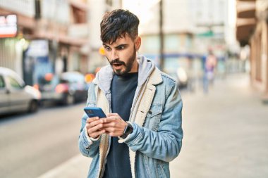 Latin kökenli genç adam sokakta akıllı telefon kullanıyor.