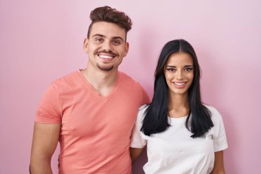 Mutlu ve havalı bir gülümseme ile pembe arka planda duran genç İspanyol çift. şanslı kişi. 