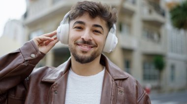 Genç Arap adam kendinden emin bir şekilde gülerek sokakta müzik dinliyor.