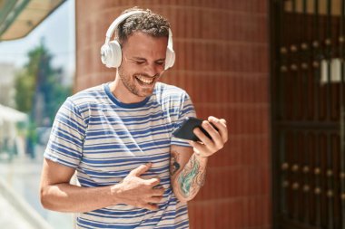 Genç İspanyol adam gülümsüyor. Sokakta akıllı telefondan videolar izliyor.