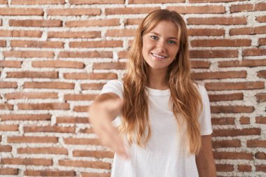 Tuğla duvarın yanında duran beyaz bir kadın dostça bir selamlama ve hoş geldin hediyesi olarak gülümsüyor. başarılı iş. 