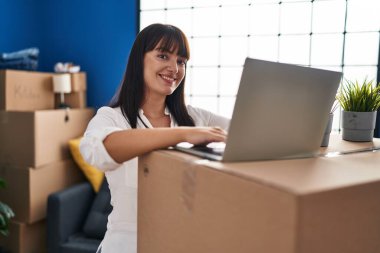 Young beautiful hispanic woman smiling confident using laptop at new home