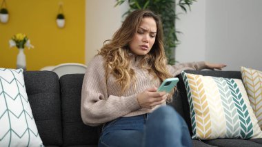 Evdeki kanepede oturan akıllı telefon kullanan genç, güzel İspanyol kadın.