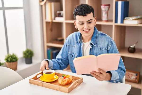 Молодой Небинарный Человек Читает Книгу Завтракая Дома — стоковое фото