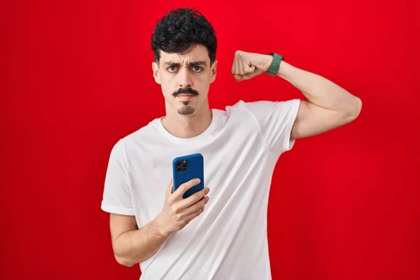 Hispanic Man Using Smartphone Red Background Strong Person Showing Arm — Stock Photo, Image