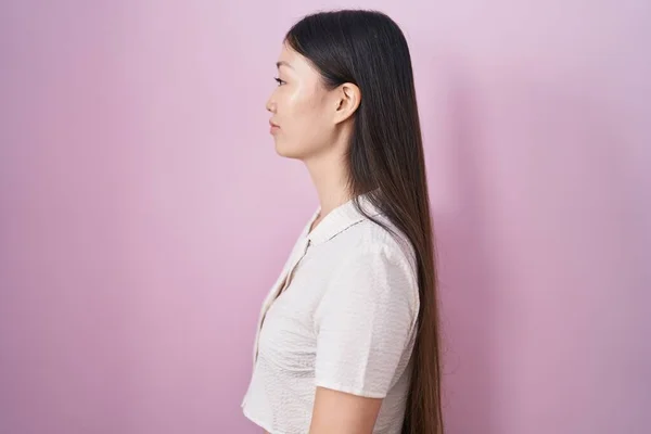 中国の若いです女性立って上のピンクの背景を見ます側に リラックスプロファイルポーズとともに自然な顔と自信に満ちた笑顔 — ストック写真