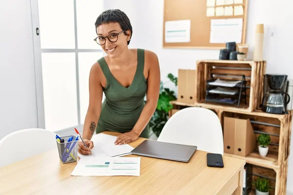 年轻的惊慌失措的女人带着自信的笑容写在办公室的文书工作上 — 图库照片