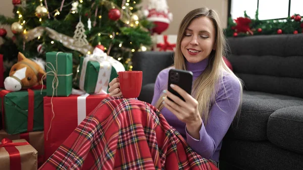 Mladá Blondýna Žena Pomocí Smartphone Pití Kávy Sedí Vánočního Stromku — Stock fotografie