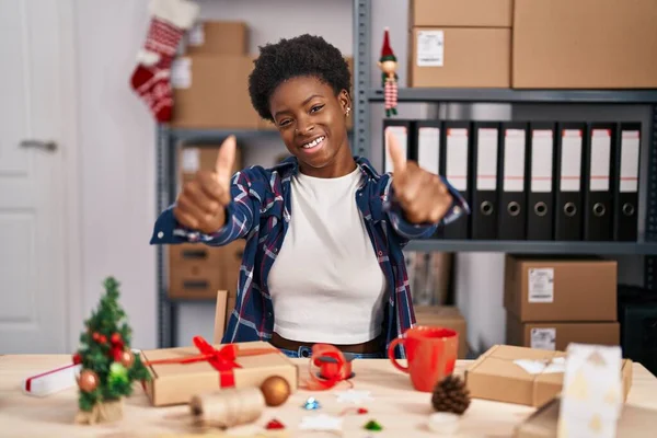 African american woman working at small business doing christmas decoration approving doing positive gesture with hand, thumbs up smiling and happy for success. winner gesture.