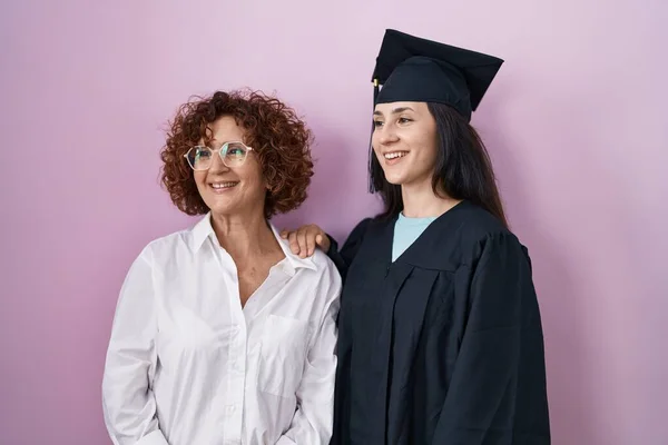顔に笑顔で横に離れて見て卒業キャップと式のローブを着てヒスパニック系の母親と娘 自然な表情 自信を持って — ストック写真