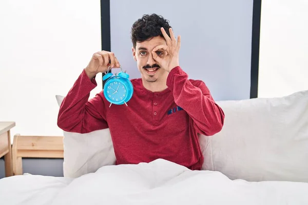Hispanic Man Håller Väckarklocka Sängen Ler Glad Gör Tecken Med — Stockfoto