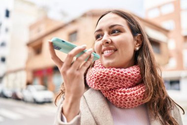 Young beautiful hispanic woman talking on smartphone wearing scarf at street