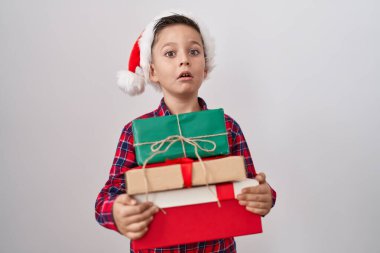 Küçük İspanyol çocuk Noel şapkası takıyor. Elinde hediyeler var. Şok olmuş bir yüz ifadesi. 