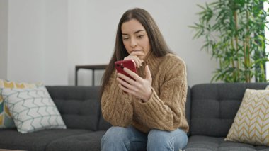 Evdeki kanepede oturan akıllı telefon kullanan genç, güzel İspanyol kadın.