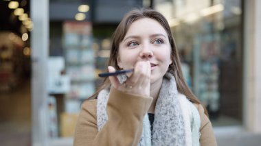 Young blonde woman smiling confident sending voice message by smartphone at street
