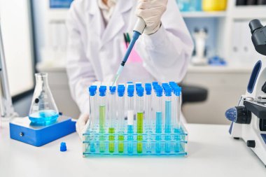 Laboratuvarda çalışan pipet kullanan bilim adamı üniforması giyen genç bir kadın.