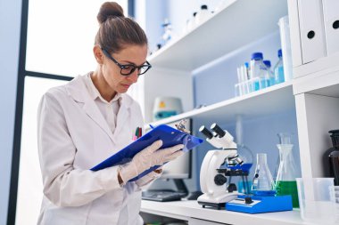 Young woman scientist measuring liquid writing on clipboard at laboratory