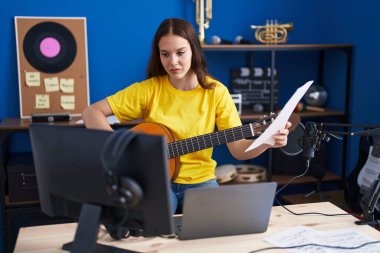 Young woman musician playing classical guitar at music studio