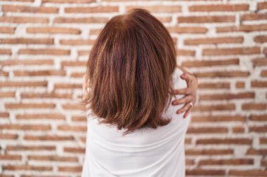 Gözlüklü yaşlı bir kadın, duvarın başında durmuş, kendine sarılıyor, mutlu ve pozitiftir. Sevgi ve özgüven. 