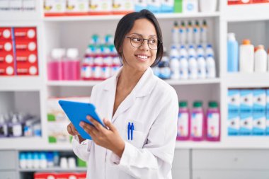 Young hispanic woman pharmacist using touchpad working at pharmacy