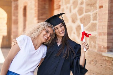 Two women mother and graduated daughter hugging each other at campus university