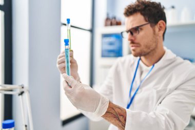 Young hispanic man scientist holding test tubes at laboratory