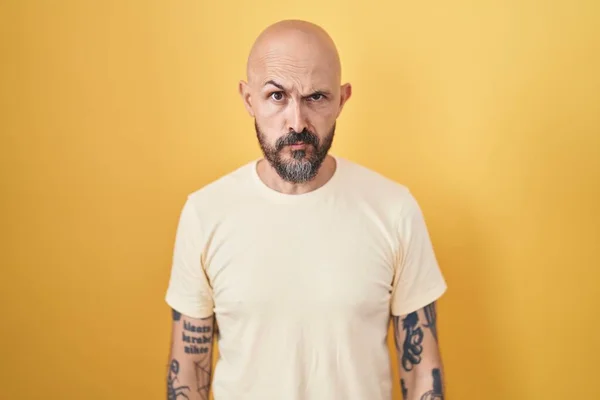 黄色の背景懐疑的で神経の上に立って入れ墨を持つヒスパニック系の男 問題のために動揺を眉をひそめて 否定的な人 — ストック写真