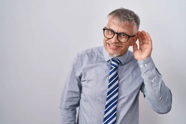 噂やゴシップに耳を傾ける耳の上に手で笑みを浮かべて眼鏡を着て灰色の髪を持つヒスパニック系のビジネスマン 聴覚障害の概念 — ストック写真