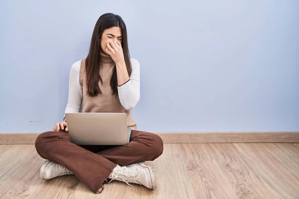 年轻的黑发女人坐在地板上 用电脑笔记本电脑工作 闻到一股难闻难闻的气味 用手指捂住鼻子屏住呼吸 — 图库照片