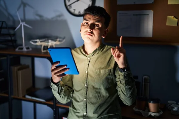 Non binary person using touchpad device at night pointing up looking sad and upset, indicating direction with fingers, unhappy and depressed.