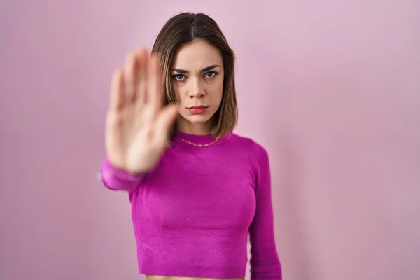 Hispanic woman standing over pink background doing stop sing with palm of the hand. warning expression with negative and serious gesture on the face.