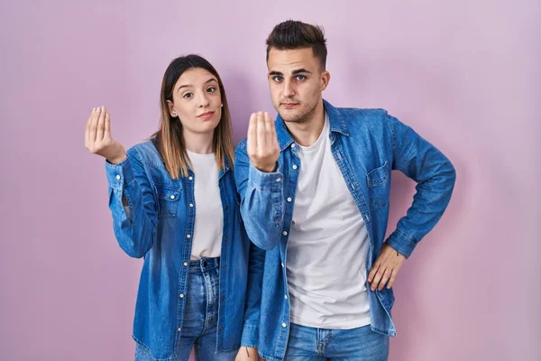 他那对年轻的惊慌失措的夫妇站在粉红的背景上 手指手画脚地做着意大利式的手势 — 图库照片