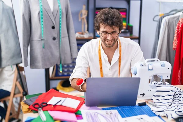 在服装厂使用笔记本电脑时 他的年轻人裁缝带着自信的笑容 — 图库照片
