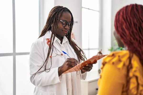 アフリカ系アメリカ人の女性医師と患者が診療所で診察報告書を書いている — ストック写真