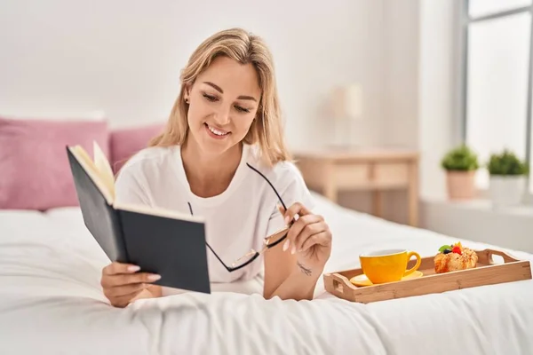 Young Blonde Woman Reading Book Having Breakfast Bedroom — 图库照片