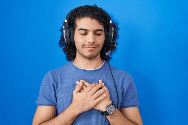 目を閉じて胸に手で笑みを浮かべてヘッドフォンを使用して音楽を聞いて巻き毛を持つヒスパニック系の男と顔に感謝のジェスチャー 健康の概念 — ストック写真