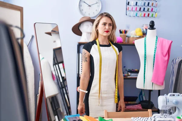 Young beautiful hispanic woman tailor standing with serious expression at clothing factory