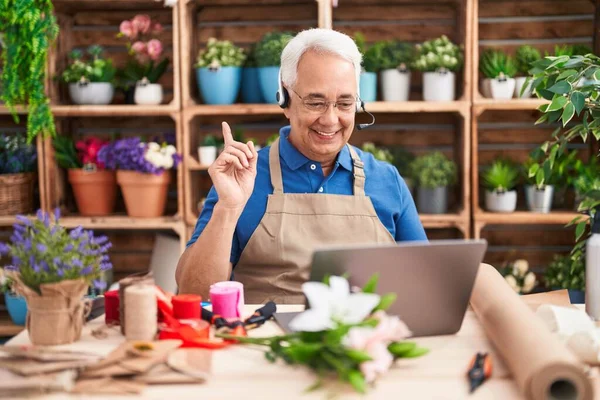 Middle age man with grey hair working at florist shop doing video call smiling happy pointing with hand and finger to the side