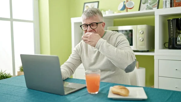 Orta Yaşlı Kır Saçlı Bir Adam Kahvaltısını Evde Dizüstü Bilgisayar — Stok fotoğraf