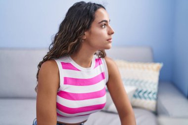 Young beautiful hispanic woman sitting on sofa with serious expression at home