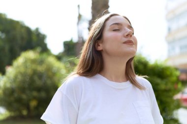 Parkta gözleri kapalı beyaz bir kadın nefes alıyor.