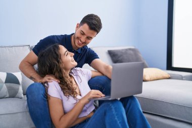 Young hispanic couple using laptop sitting on sofa at home