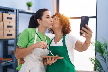 Sanat stüdyosunda iki kadın sanatçı akıllı telefon çizimiyle selfie çekiyor.