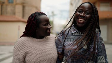 İki Afro-Amerikalı arkadaş gülerek sokakta bir arada duruyorlar.