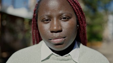 Örgülü saçlı Afrikalı kadın sokakta ciddi bir ifadeyle ayakta duruyor.