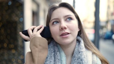 Young blonde woman smiling confident listening audio message by the smartphone at street