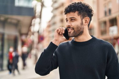 Genç Arap adam gülümsüyor, kendinden emin bir şekilde caddedeki akıllı telefondan konuşuyor.